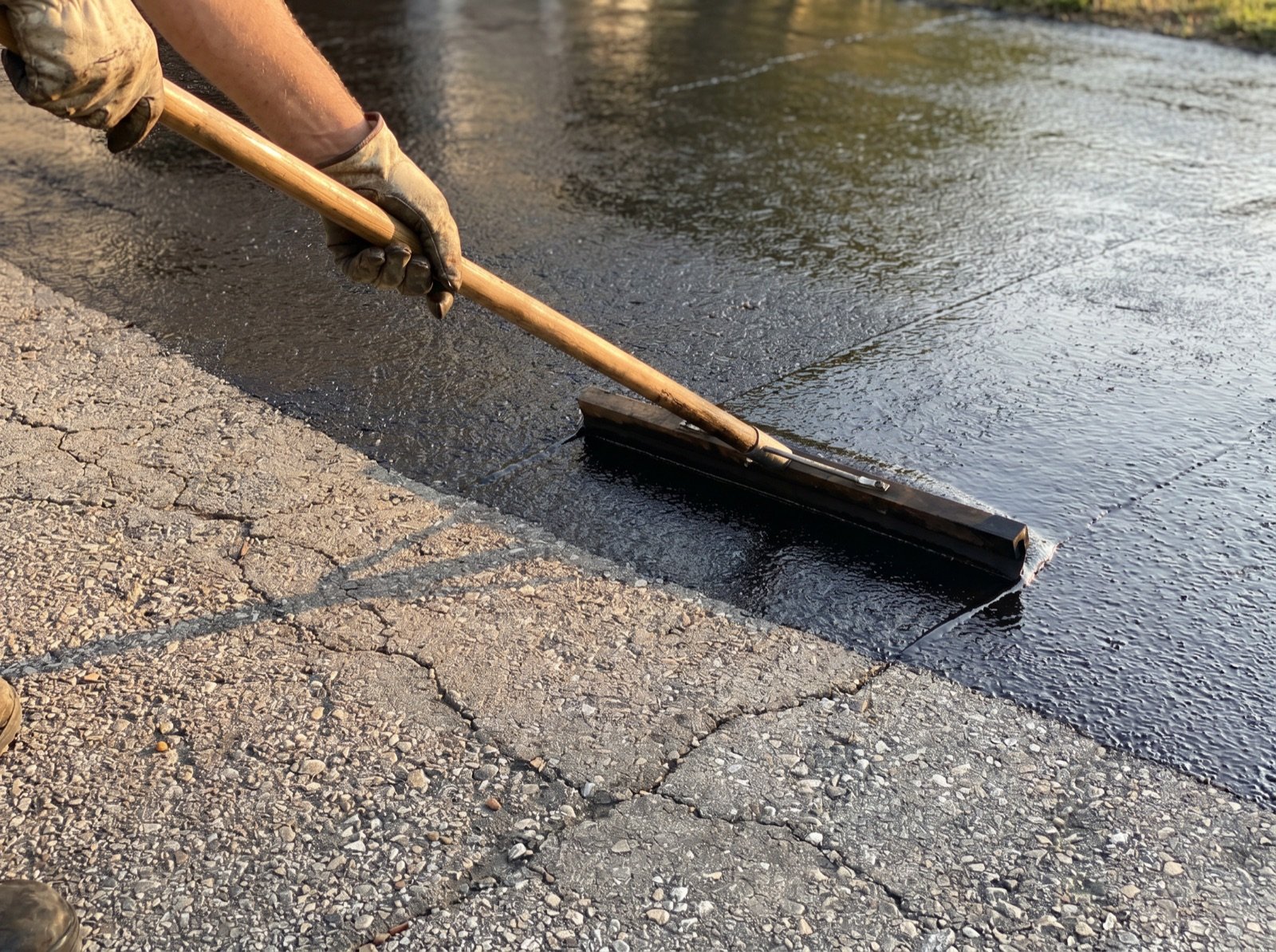 Squeegee spreading glossy black sealcoat across a driveway