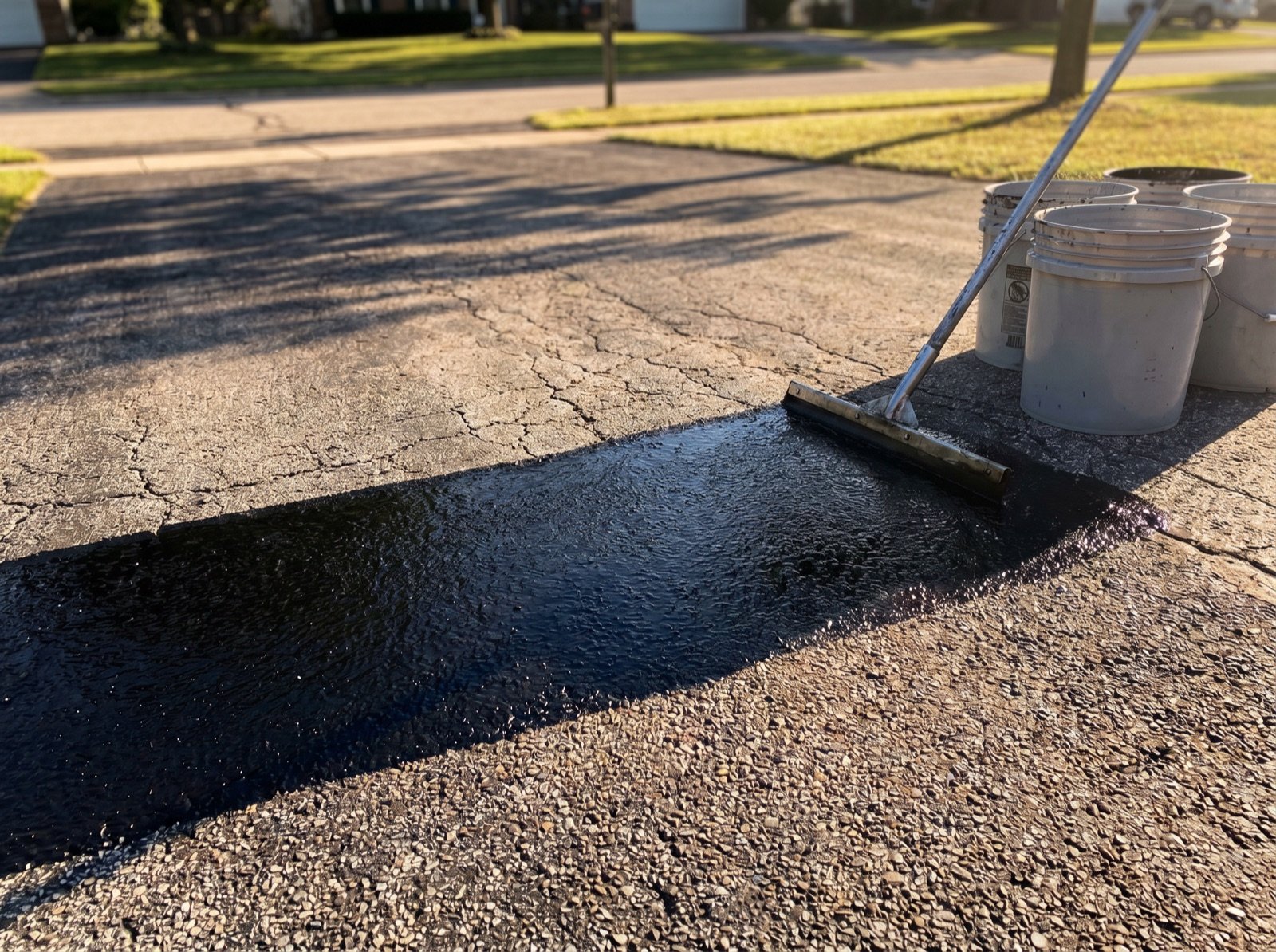 Fresh black sealcoat laid over cracked, weathered gray asphalt